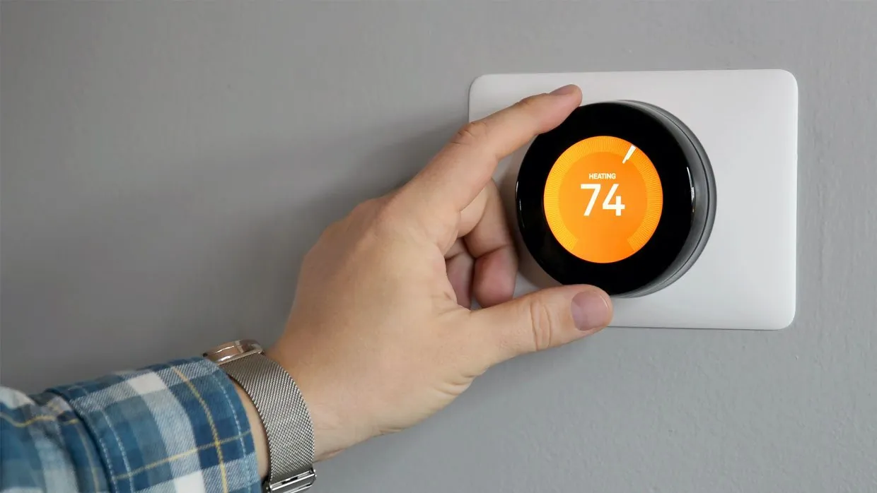 Hand adjusting a smart thermostat set to 74 degrees