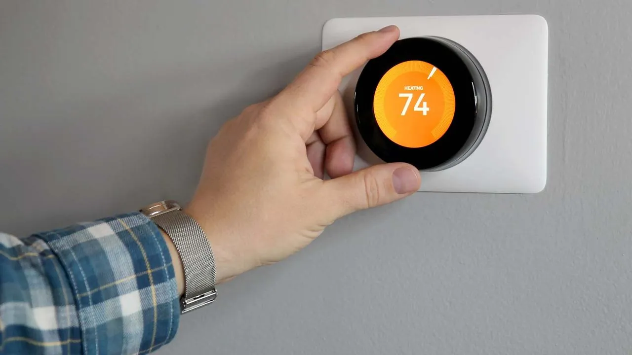 Hand adjusting a smart thermostat set to 74 degrees