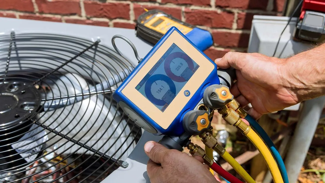 Technician connecting digital refrigerant gauges to an AC condenser