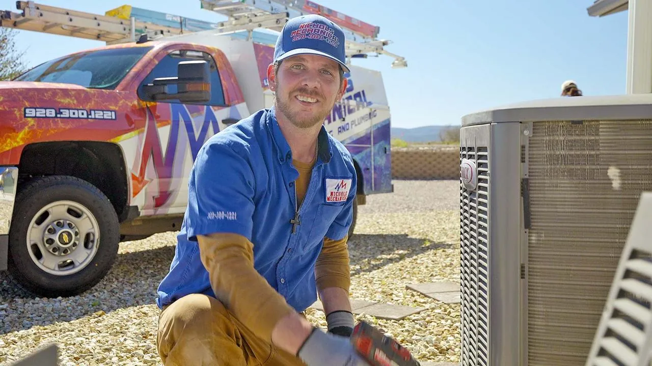 Nichols technician kneeling beside an AC condenser with his service truck behind him