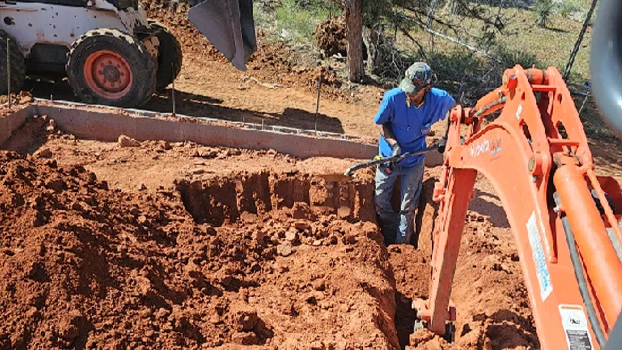 Plumber working in an excavated trench beside a backhoe
