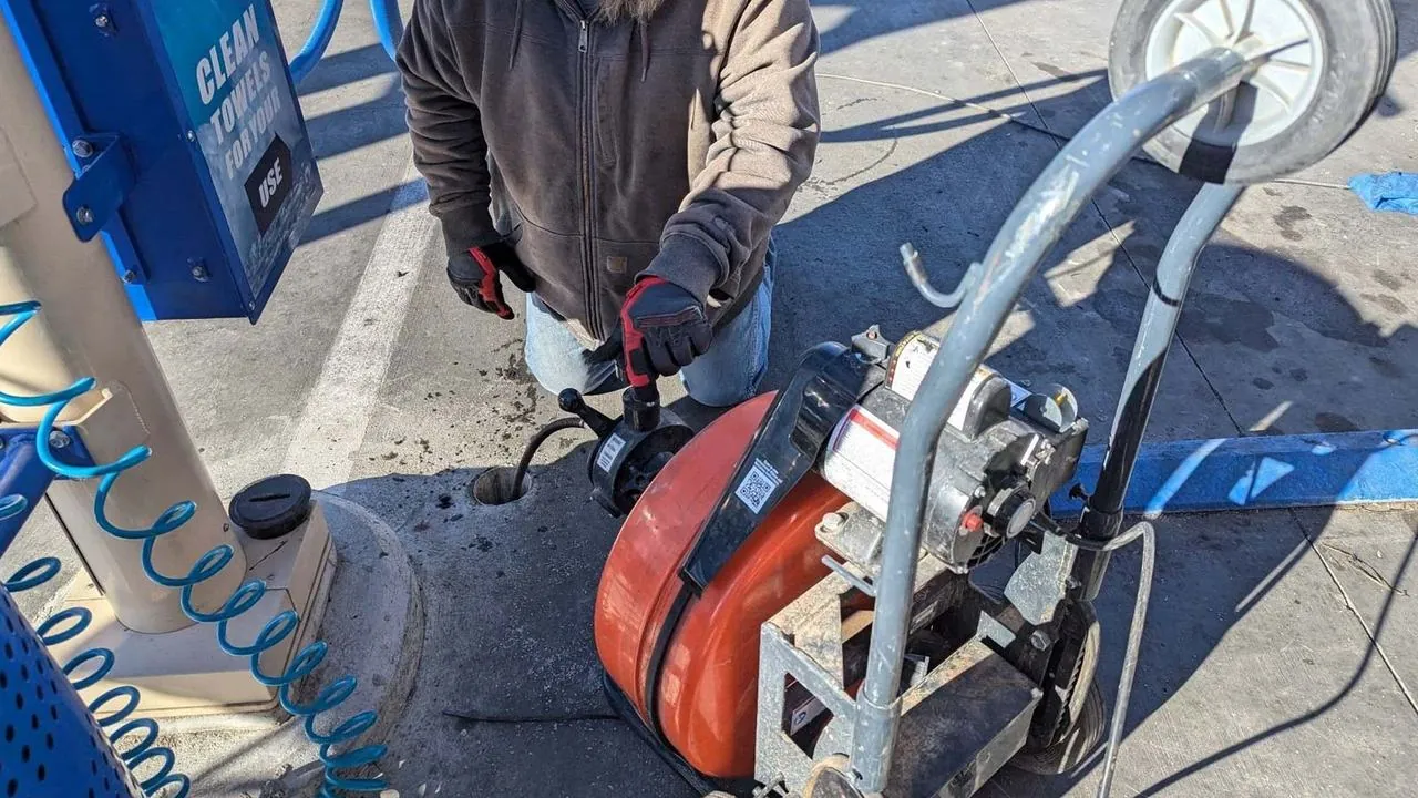 Plumber running a drain snake machine at a car wash