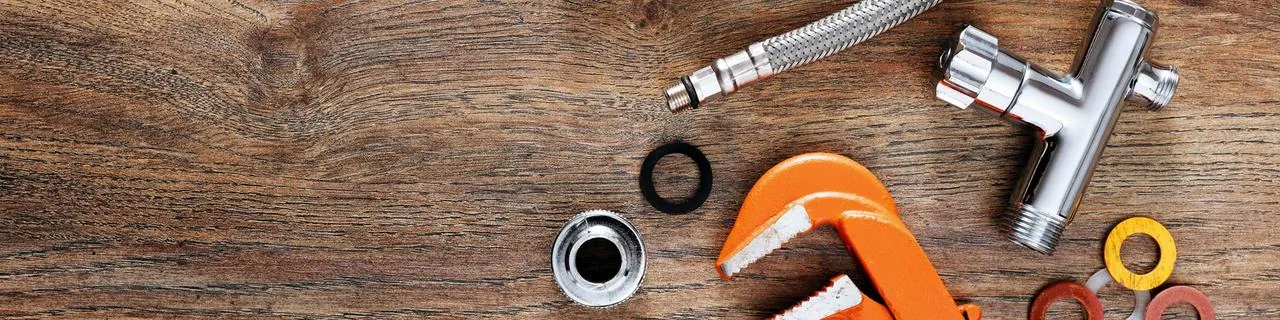 Plumbing wrench, fittings and a supply line on a wood surface