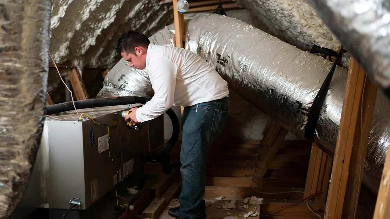 Technician servicing an air handler and ductwork in an attic