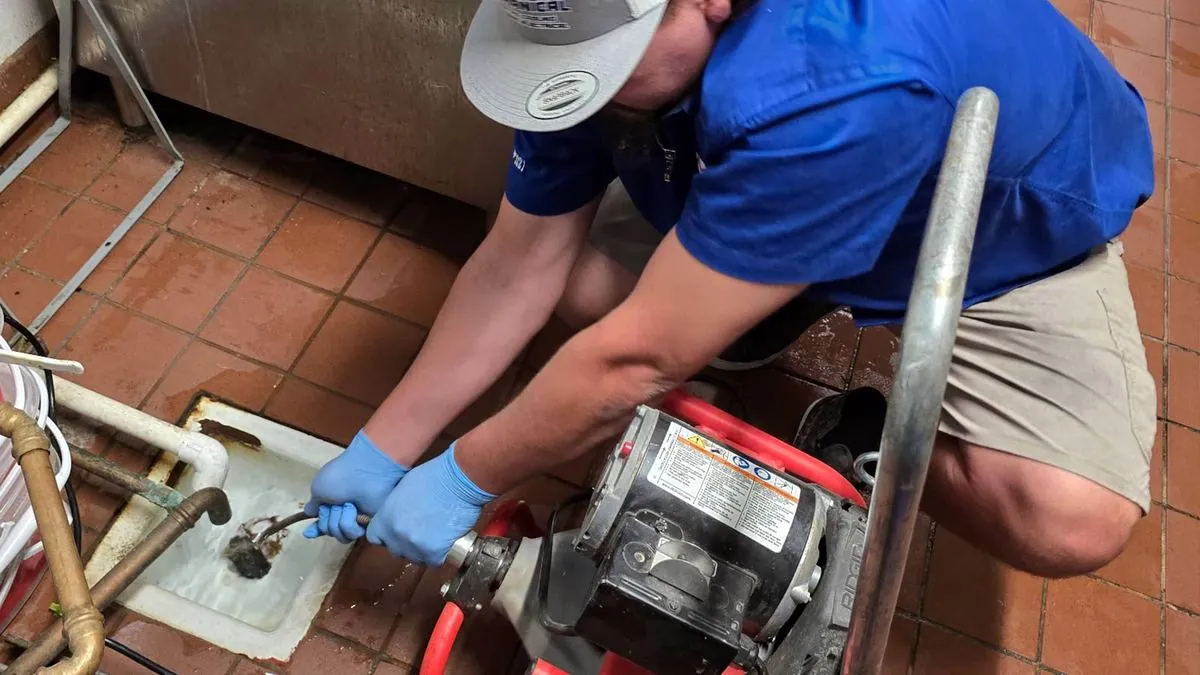 Nichols plumber clearing a commercial kitchen floor drain with a drain machine