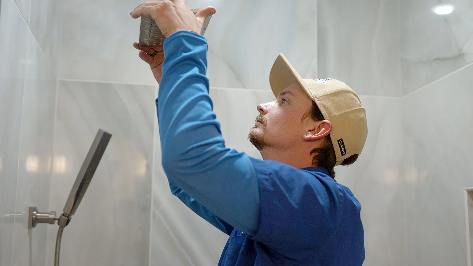 Plumber installing a shower head in a tiled shower