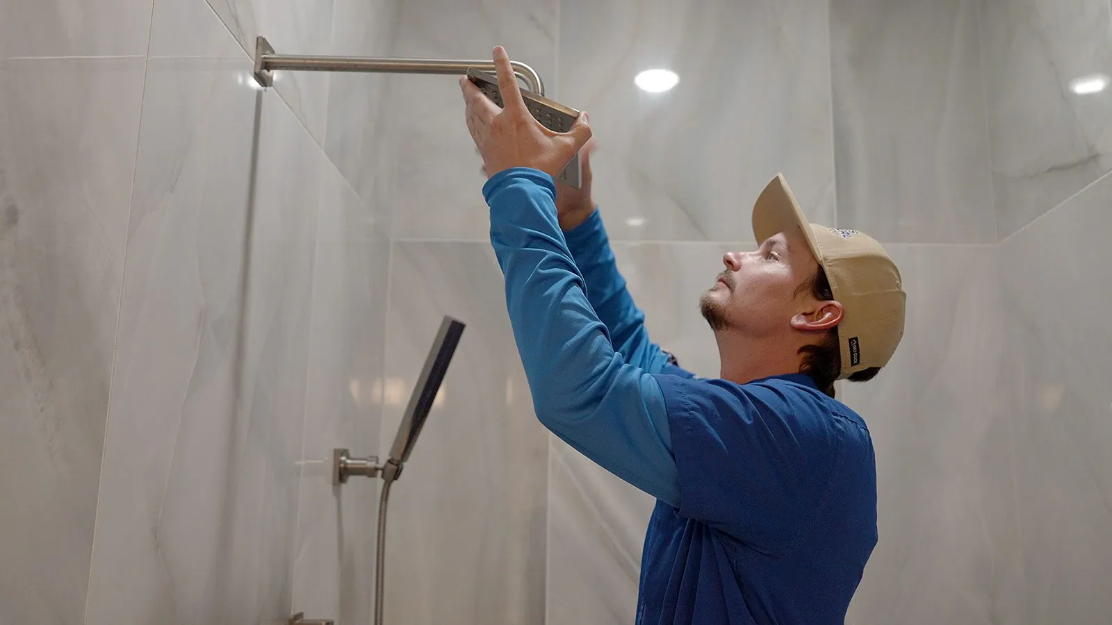 Plumber repairing a shower arm in a tiled shower