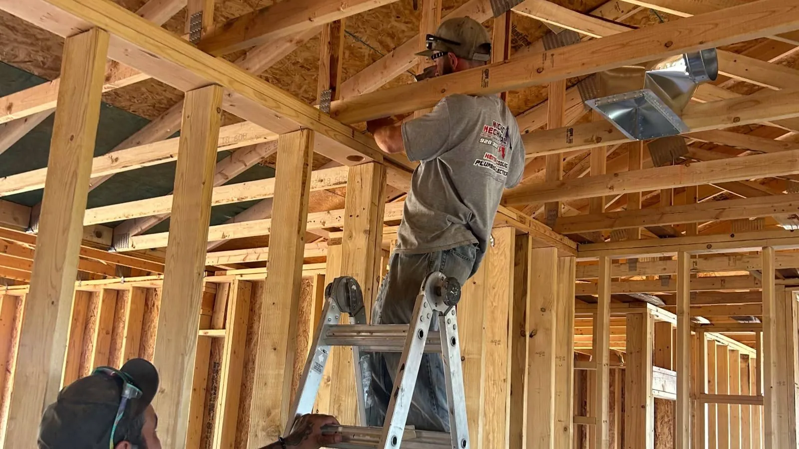 Technician on a ladder installing ductwork in a new home's framing