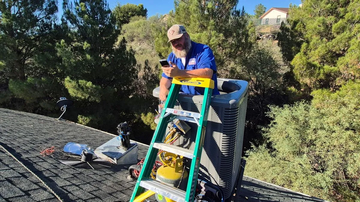 Nichols technician on a ladder servicing a rooftop AC unit in Prescott